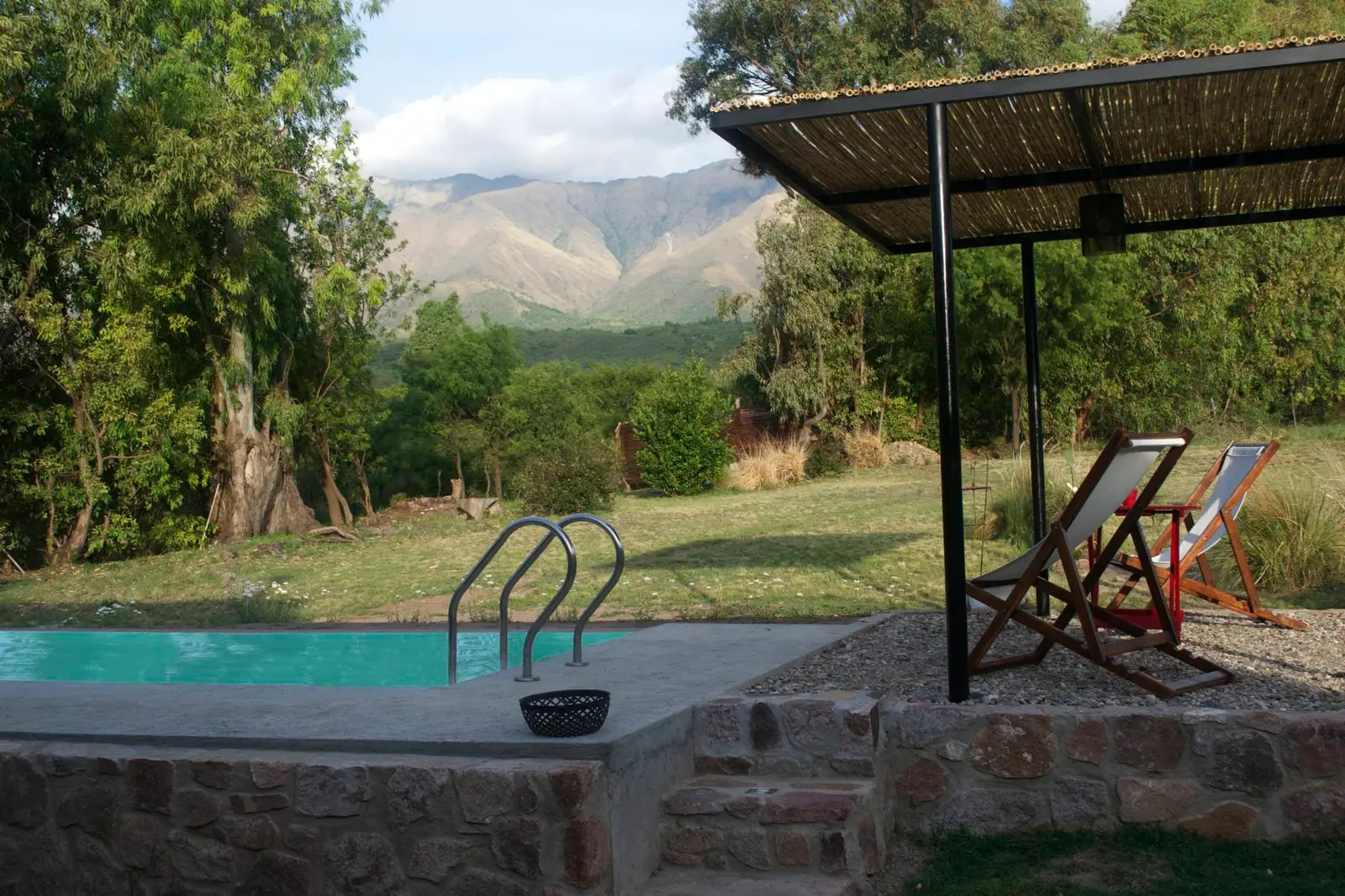 Pileta con reposeras bajo una pérgola y vista a las sierras